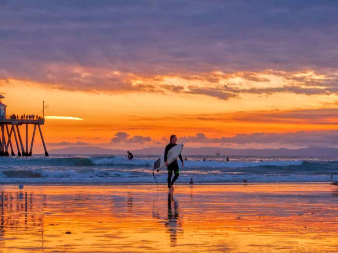 Surfer walks the sand at sunset near Huntington Beach Pier, Surf City USA